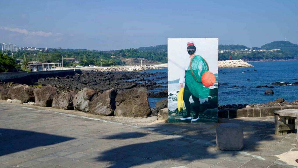 A haenyeo photo board stands by Beophwan’s volcanic shore.