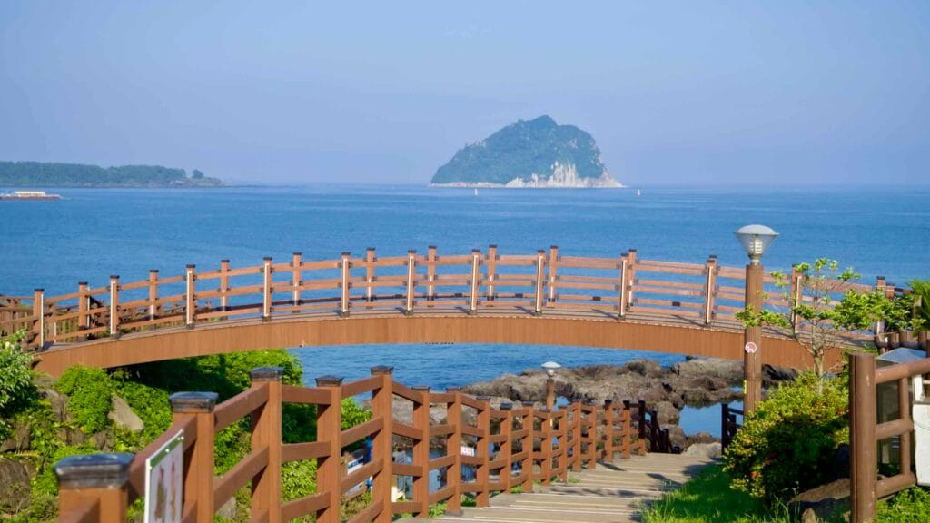 A wooden footbridge on the Jaguri coastal walk crosses the rocks with Seopseom Island beyond.
