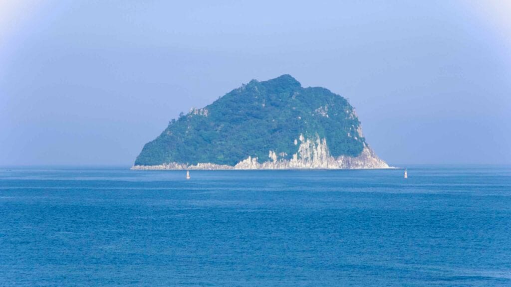 Seopseom Island rises from calm blue water off Seogwipo, with forested slopes and pale cliffs.