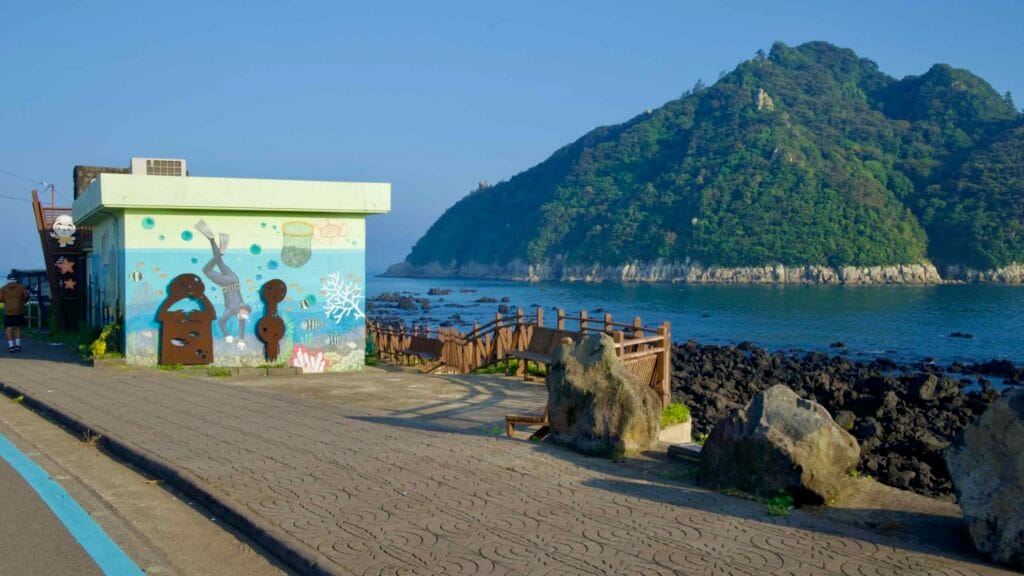 A haenyeo mural marks the Jaguri walk with Seopseom Island beyond.