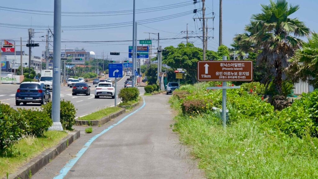 A tourist sign points toward Phoenix Island as cars pass an SK station on Iljudong Road.