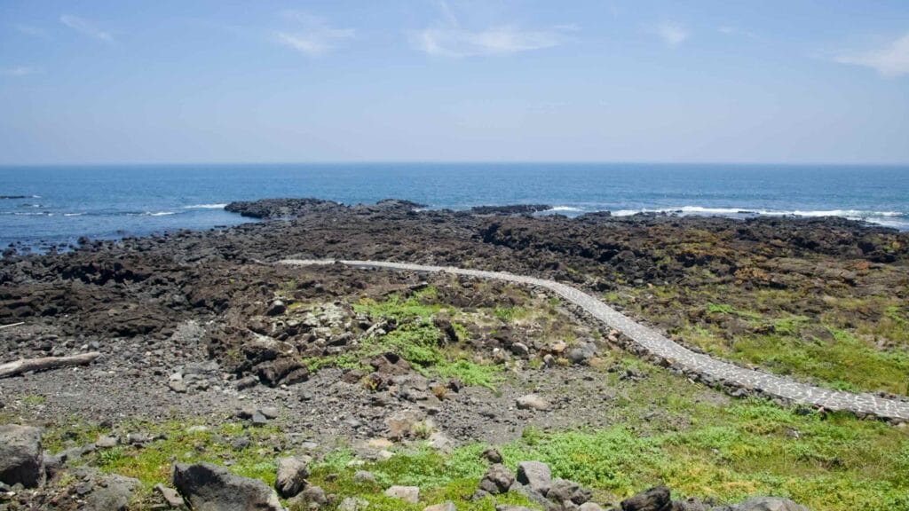 A narrow stone path crosses basalt rocks toward tide pools on Jeju’s east coast.
