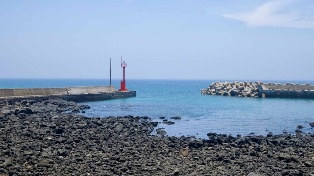 A red harbor light stands at the jetty while tetrapods guard the channel on Jeju’s coast.