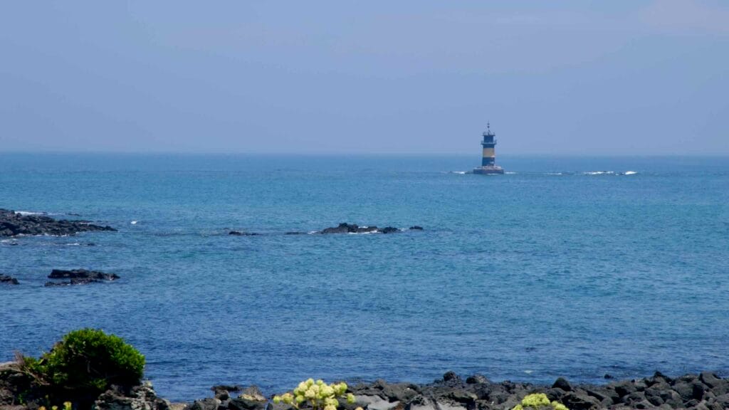 An offshore lighthouse rises beyond the lava shore at Onpyeong.