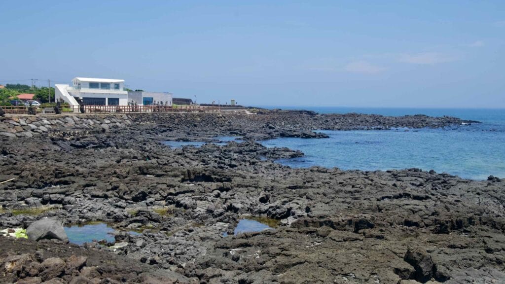 Lava platforms front a seafront walkway and village buildings.