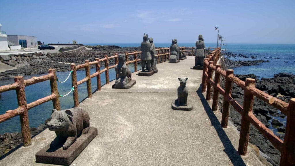 Basalt figures and animals line a pier above the water.