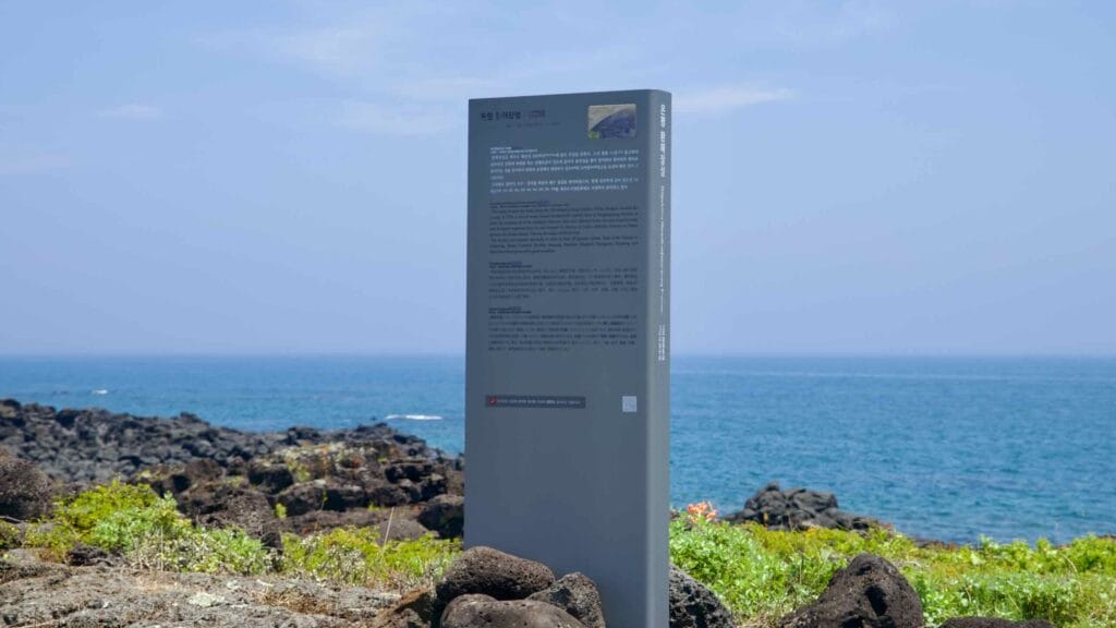 An information pillar for the Onpyeong Hwanhaejangseong stands above the basalt shore.