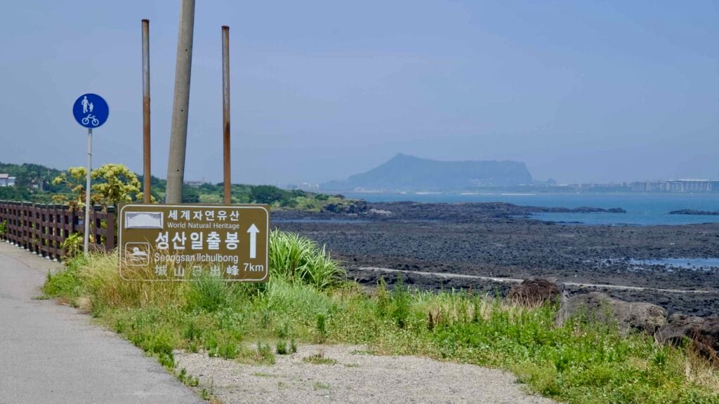 A coastal sign points to Seongsan Ilchulbong across black lava flats and tidal pools.