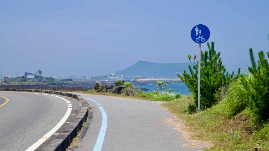A shared path with a bicycle sign follows the coast toward Sinyang and Seongsan Ilchulbong.