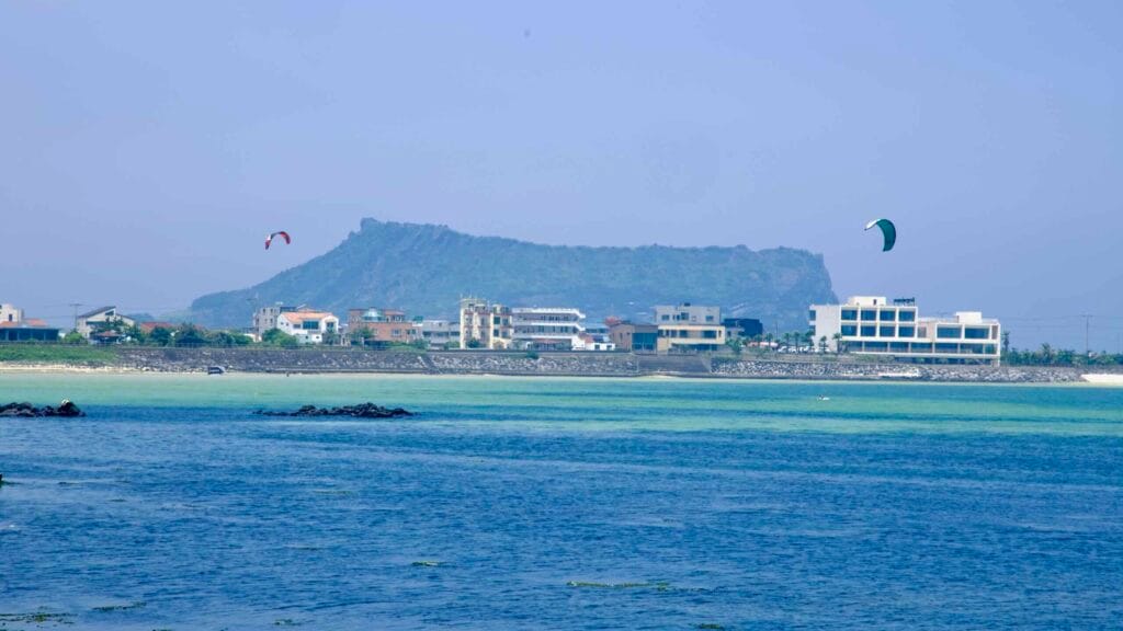 Kitesurfers ride the shallow lagoon off Sinyang Beach with Seongsan Ilchulbong beyond.