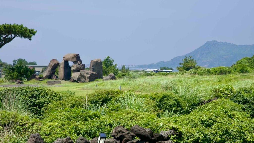 A megalithic‑style stone sculpture stands on resort grounds with Seongsan Ilchulbong beyond.
