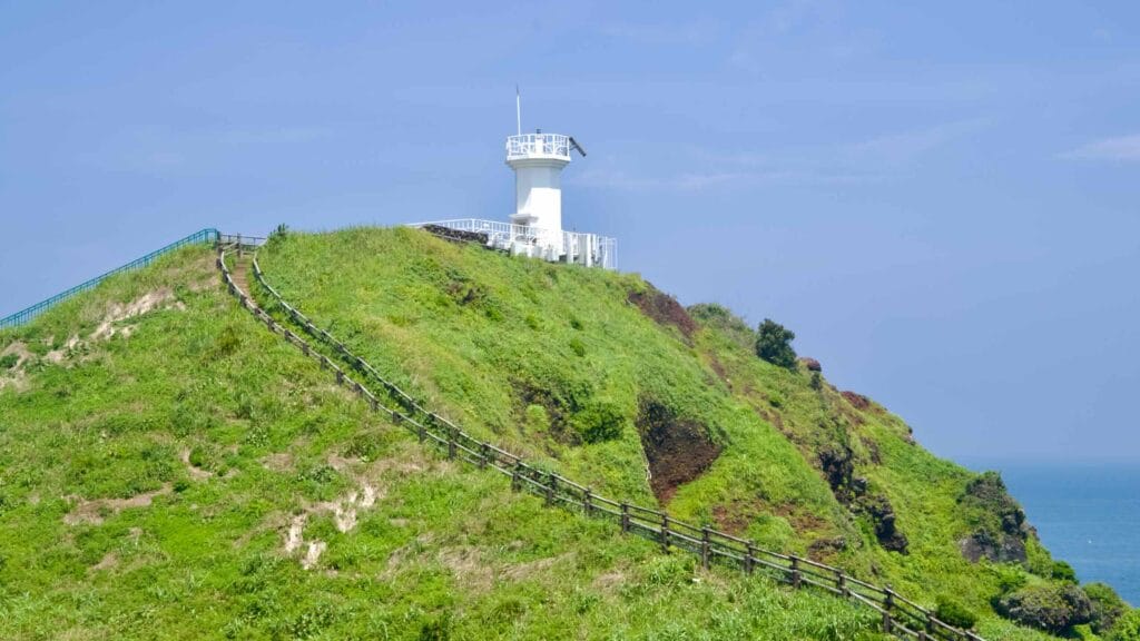 A steep stairway climbs the grassy slope to the Seopjikoji lighthouse above the sea.