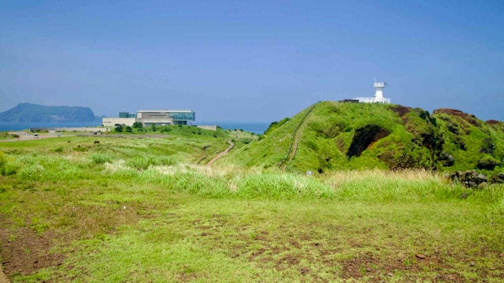 A compact white lighthouse sits above grassy volcanic slopes at Seopjikoji.