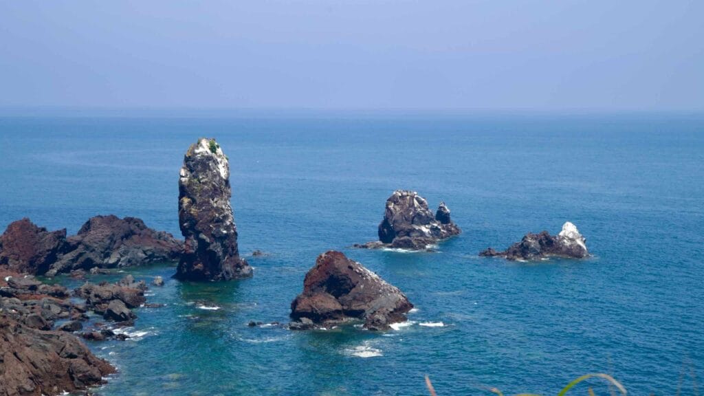 Sea stacks at Seopjikoji, including Standing Rock, rise from clear water below lava cliffs.