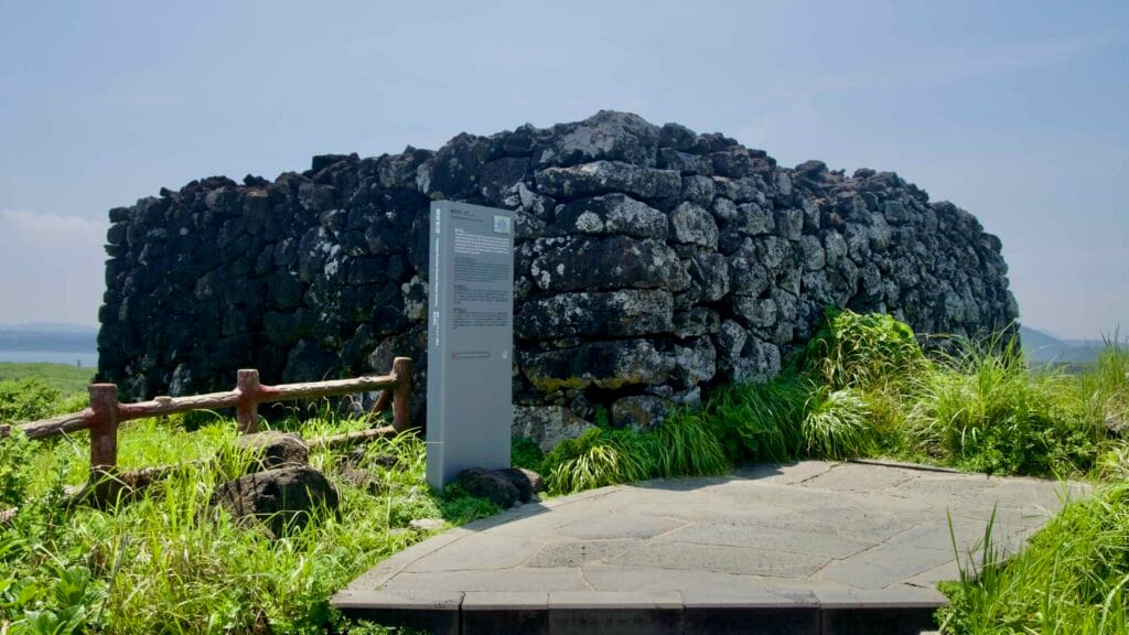 A circular basalt beacon mound from the Joseon signal network stands over the coast at Seopjikoji.