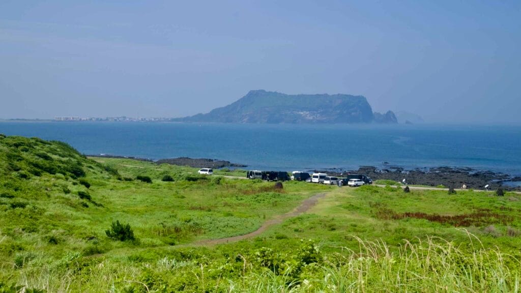Cars line the lava shore as Seongsan Ilchulbong rises across the bay.