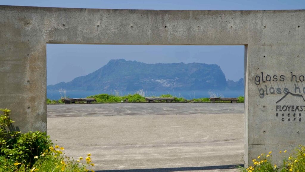 A concrete frame at the Glass House captures Seongsan Ilchulbong across the water.
