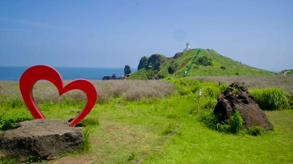 A red heart sculpture stands beneath Seopjikoji’s lighthouse with Standing Rock offshore.