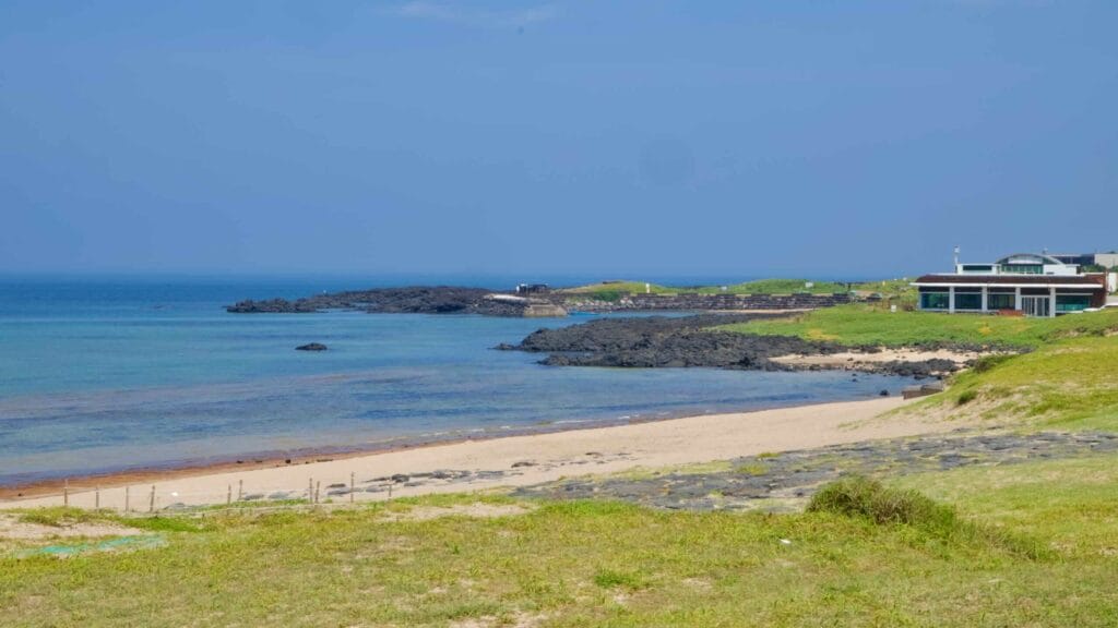 A quiet beach and lava points curve along the Seopjikoji coast beside a modern café.