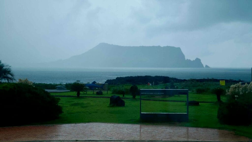 Seongsan Ilchulbong looms across the sea from the Aqua Planet Jeju grounds in the rain.