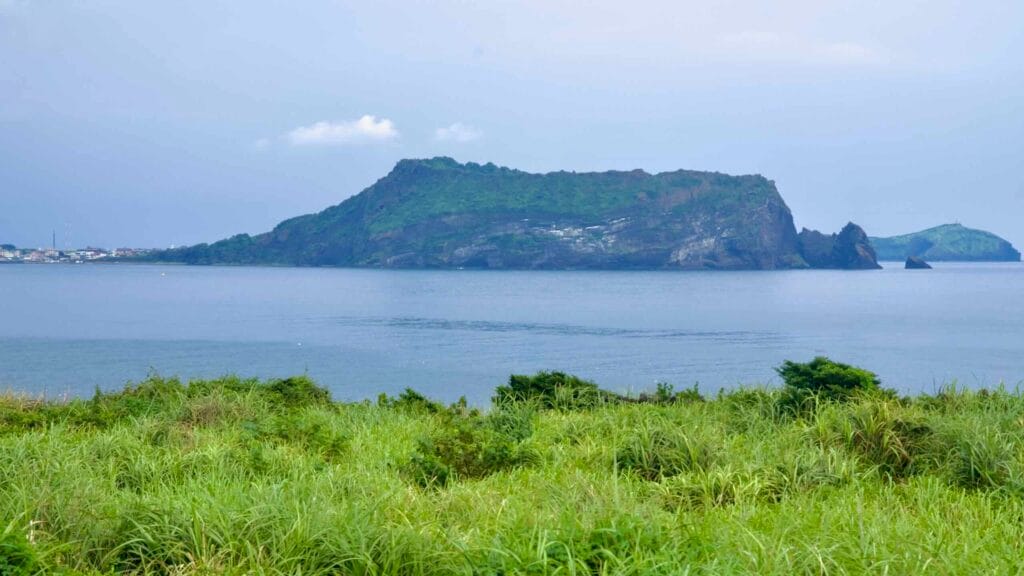 Seongsan Ilchulbong rises across the bay from Sopjikoji, its layered tuff cliffs forming a distinct profile above.