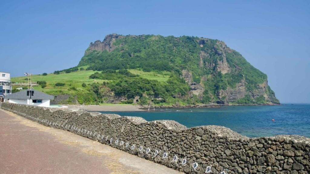 Seongsan Ilchulbong rises beyond a basalt seawall on Jeju’s eastern coast.