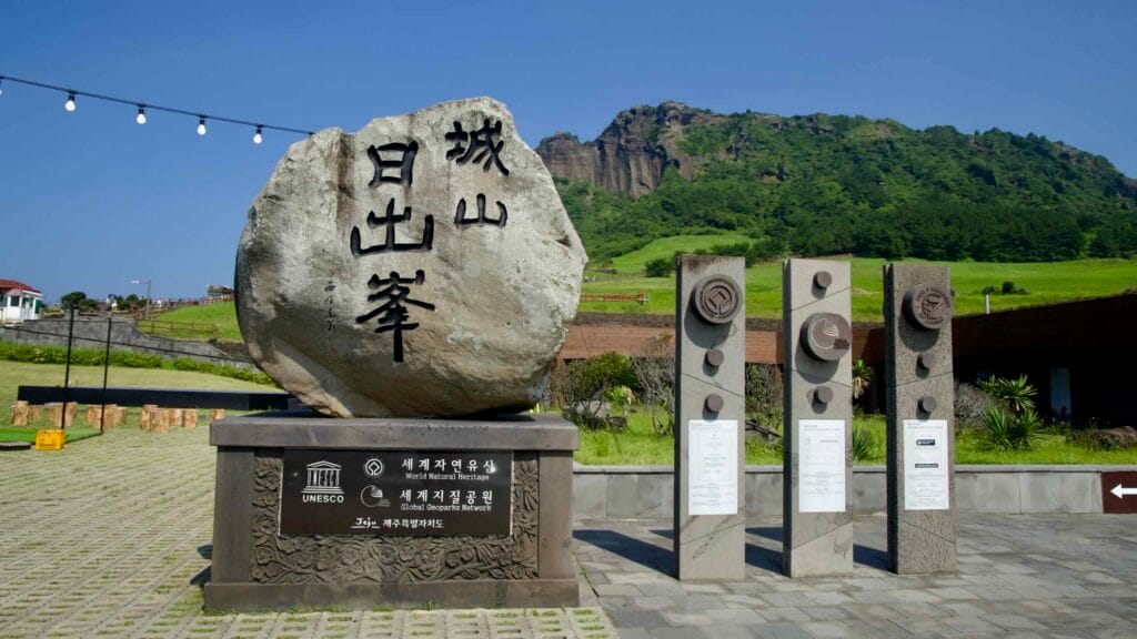 An inscribed stone and geopark pillars mark Seongsan Ilchulbong’s UNESCO World Heritage status.