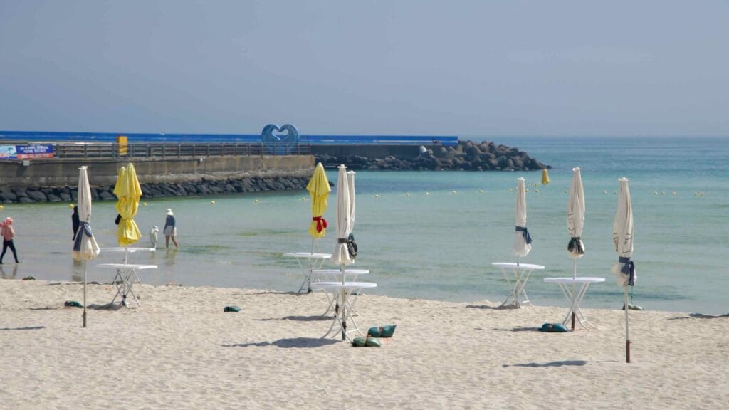 Folded parasols and a blue breakwater frame Woljeongri’s beach.