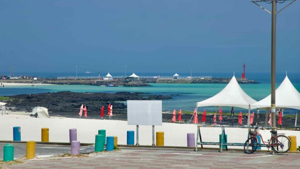 White sands and red umbrellas face a turquoise lagoon at Gimnyeong Seongsegi Beach.