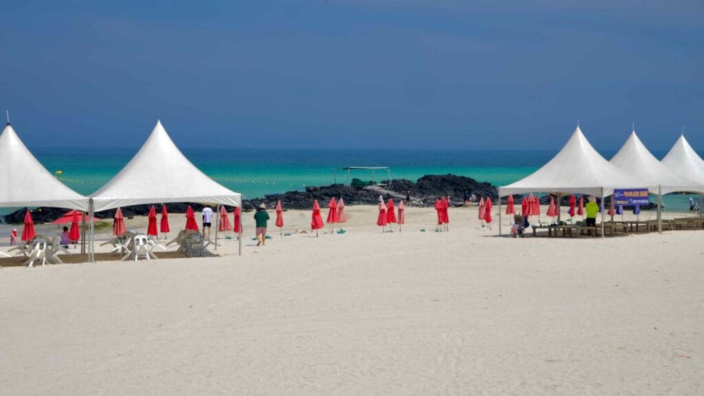 White canopies and red umbrellas face emerald waters at Gimnyeong Seongsegi Beach.