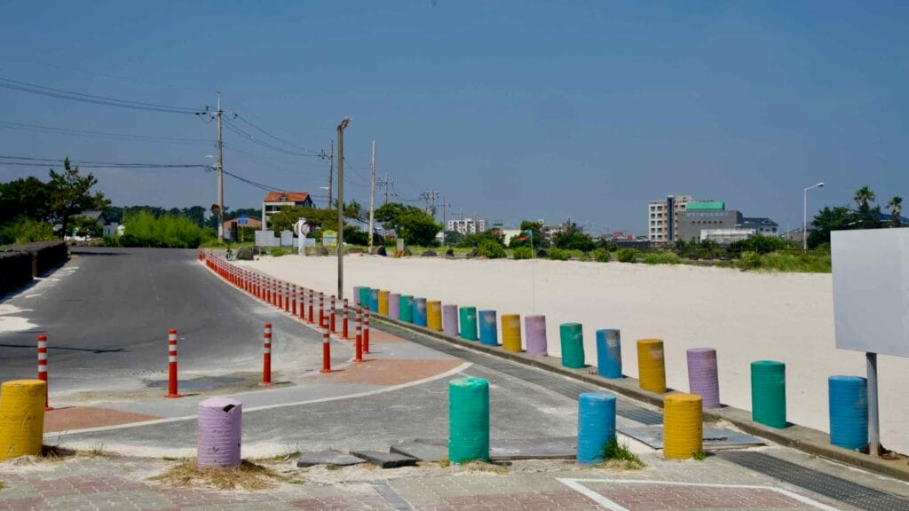 Color‑painted bollards line the access road beside the white sands at Gimnyeong.