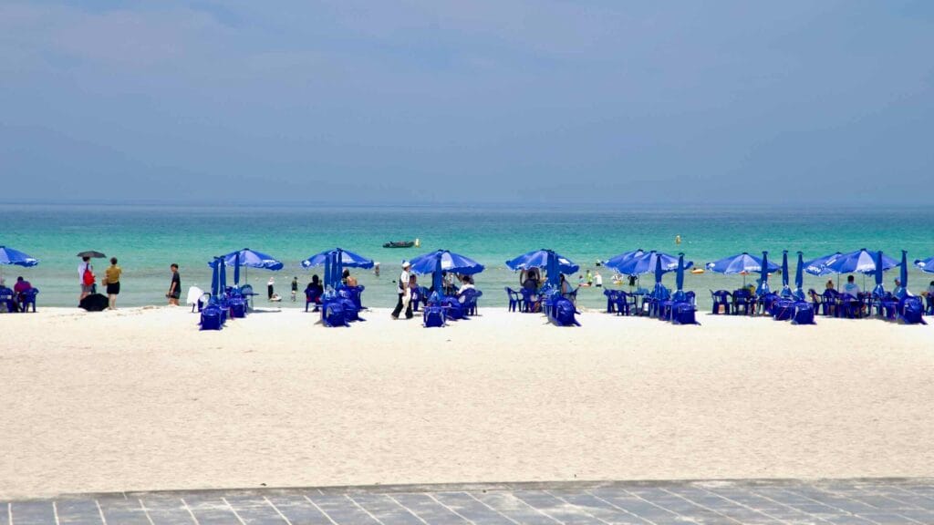 Blue umbrellas and plastic chairs dot the white sand at Hamdeok Seoubong Beach.