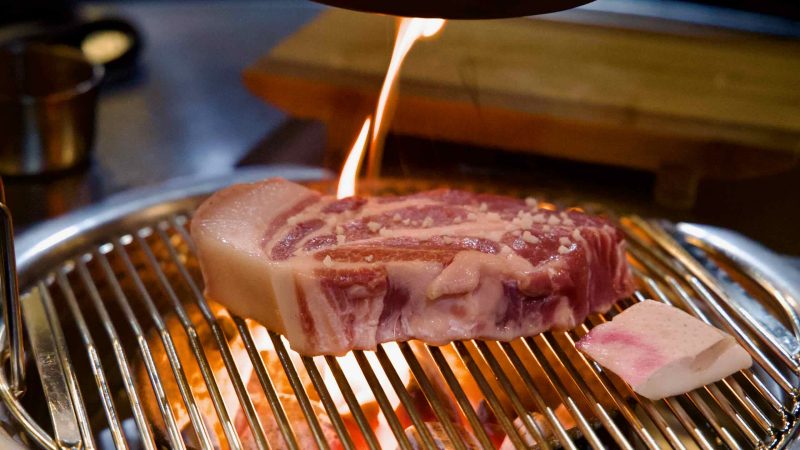 A flare kisses Jeju black pork on the charcoal grill.