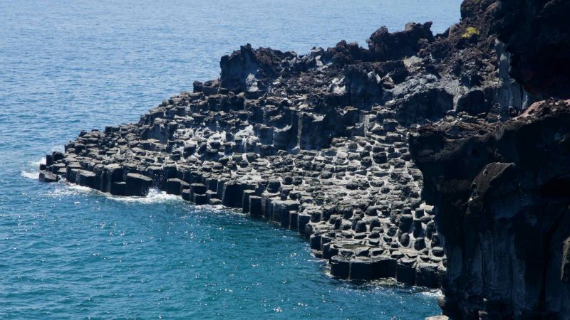 Stepped basalt shelves rise beneath a dark volcanic wall at Jusangjeolli.