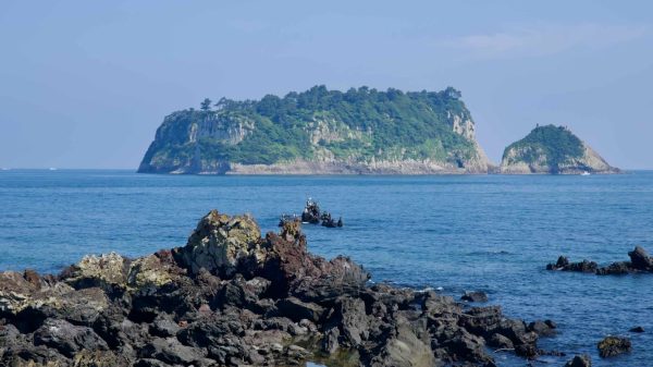 Basalt rocks fill the shore as Beomseom and its islet sit across calm seas.