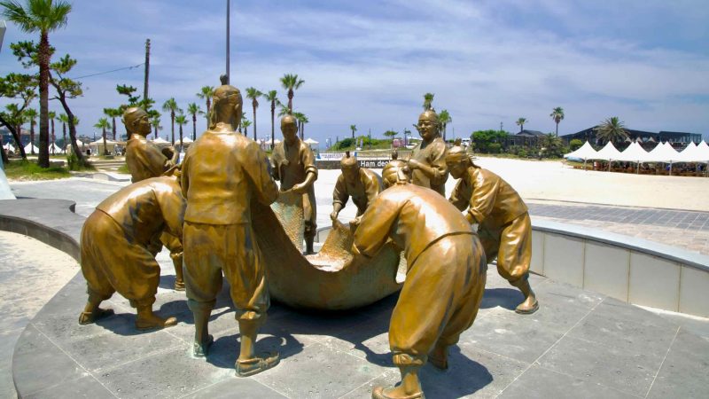 A bronze sculpture group depicts fishermen hauling a net on Hamdeok’s beachfront plaza.