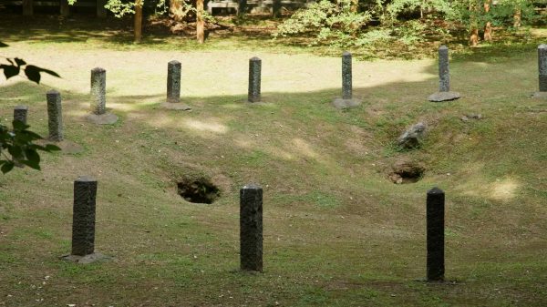 Short stone posts encircle the three sacred holes of Samseonghyeol inside a grassy basin.