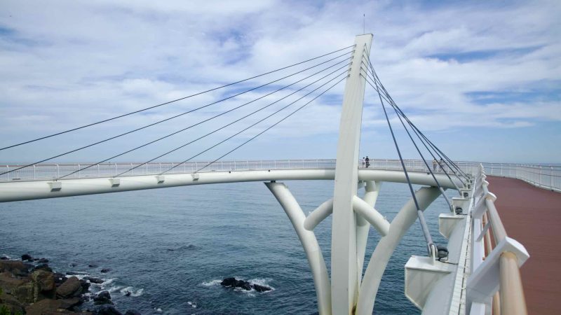 View from deck along white cable‑stayed pedestrian bridge over the sea.