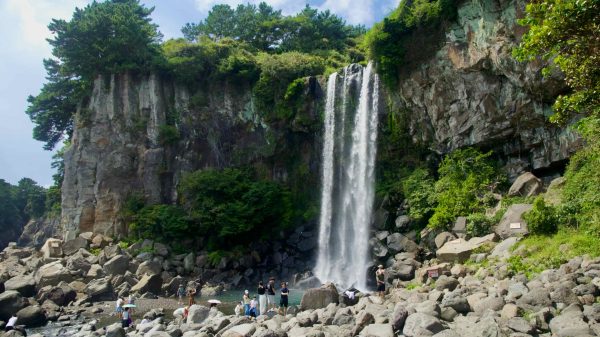 Visitors gather on boulders at the base of Jeongbang Falls.