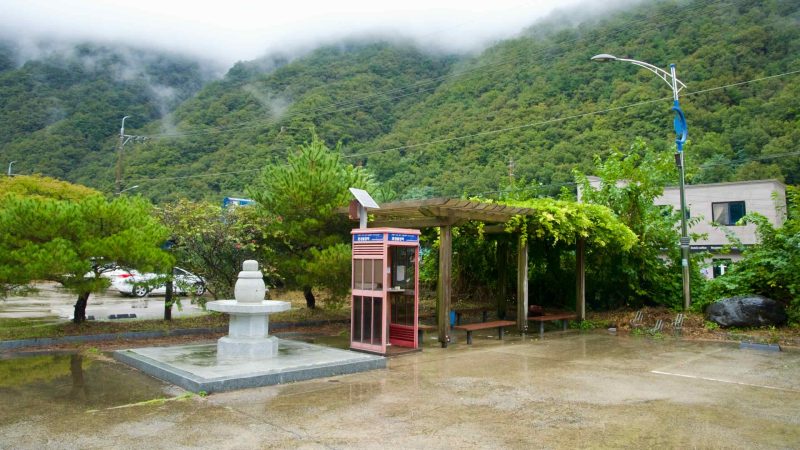 Rain falls at Buljeong Station’s stamp booth and shelter under misty hills.