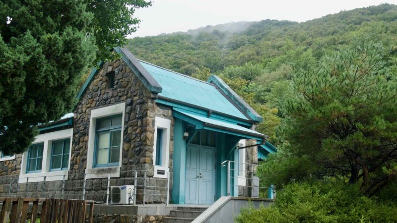 Fieldstone Buljeong Station with a turquoise roof nestles below misty hills.