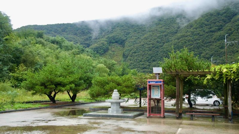 A stamp booth, stone pagoda, and pergola stand at Buljeong Station after rain.