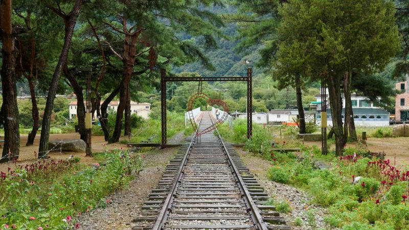 Another heart frame arches above disused tracks that reach a narrow bridge by village homes.