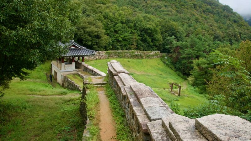 A wall walk crosses a gatehouse at Gomo Mountain Fortress in drifting mist.