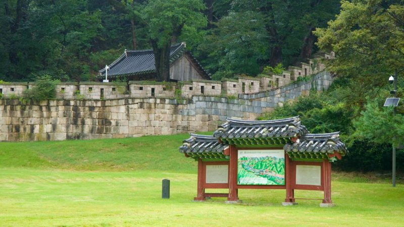 A traditional-roofed information board stands below stepped ramparts at Mungyeong Saejae.