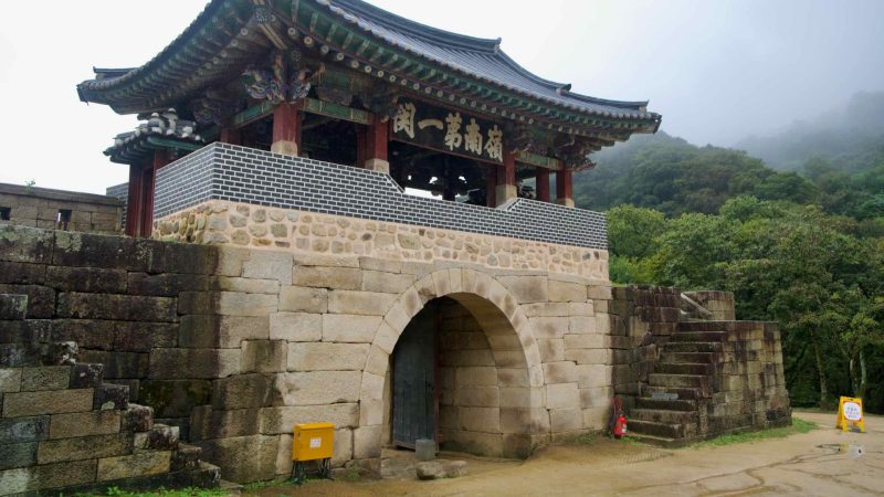 A gatehouse pavilion and stone steps emerge from fog at Mungyeong Saejae.