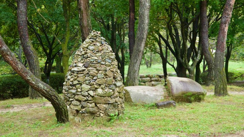 A conical stone cairn stands between pines at Mungyeong Saejae Provincial Park.