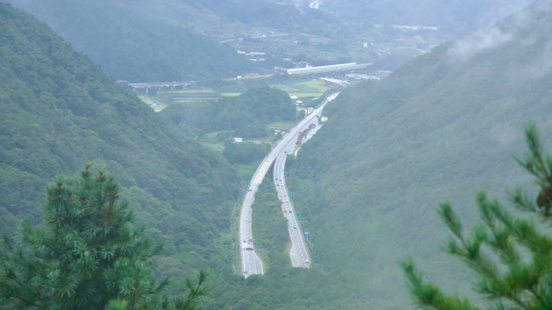 A highway winds through a forested valley below Ihwa Pass after rain.
