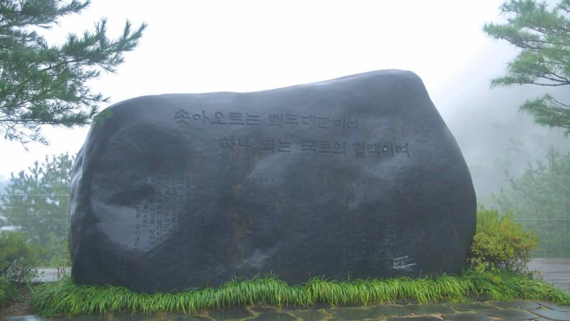 An inscribed boulder stands on the deck at foggy Ihwa Pass.