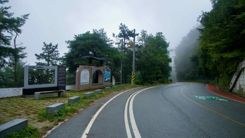 The Saejae Bike Path stamp and frame stand beside the foggy road at Ihwa Pass.
